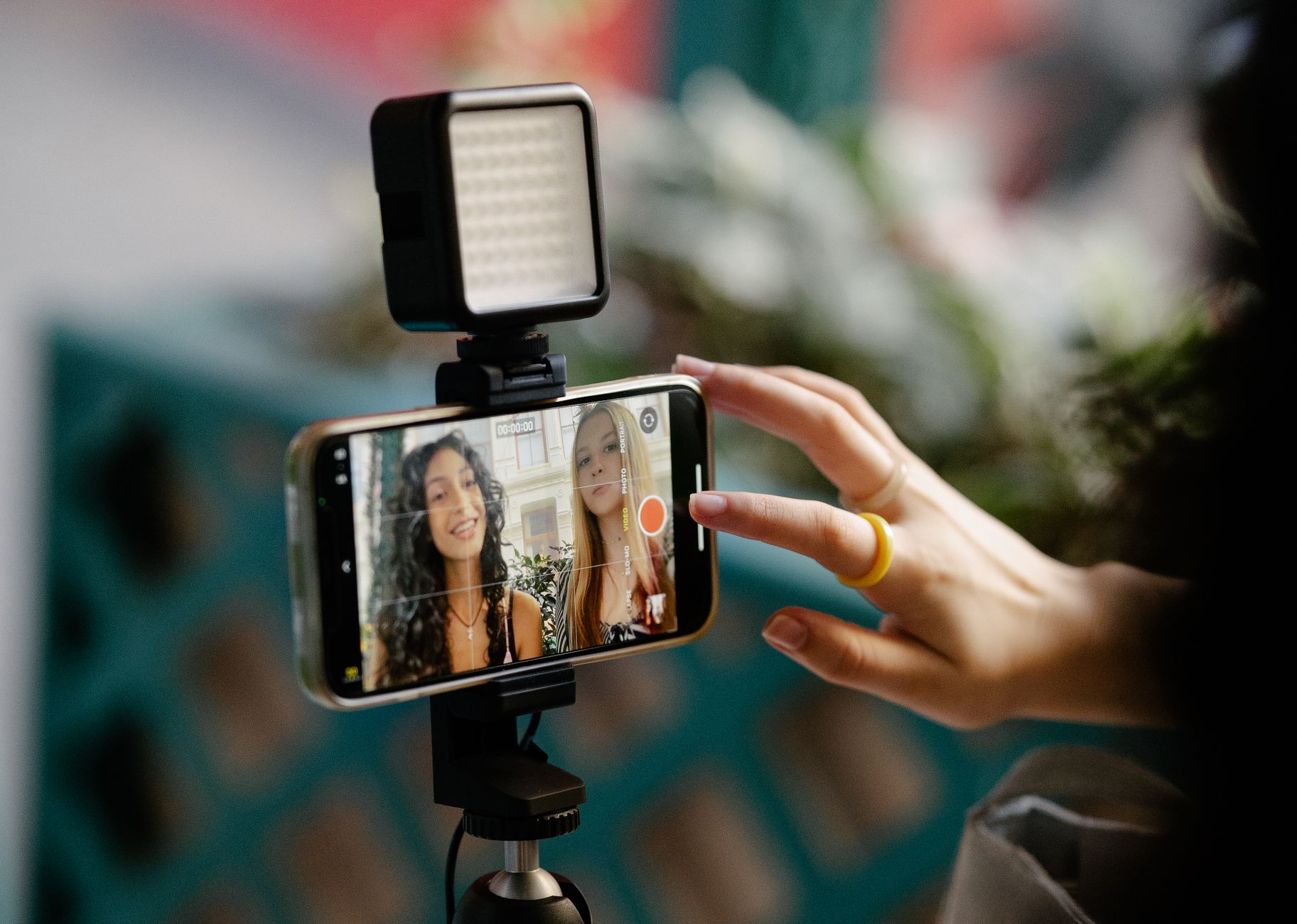 Two women recording a video together using a smartphone and an LED light setup, illustrating modern content creation.