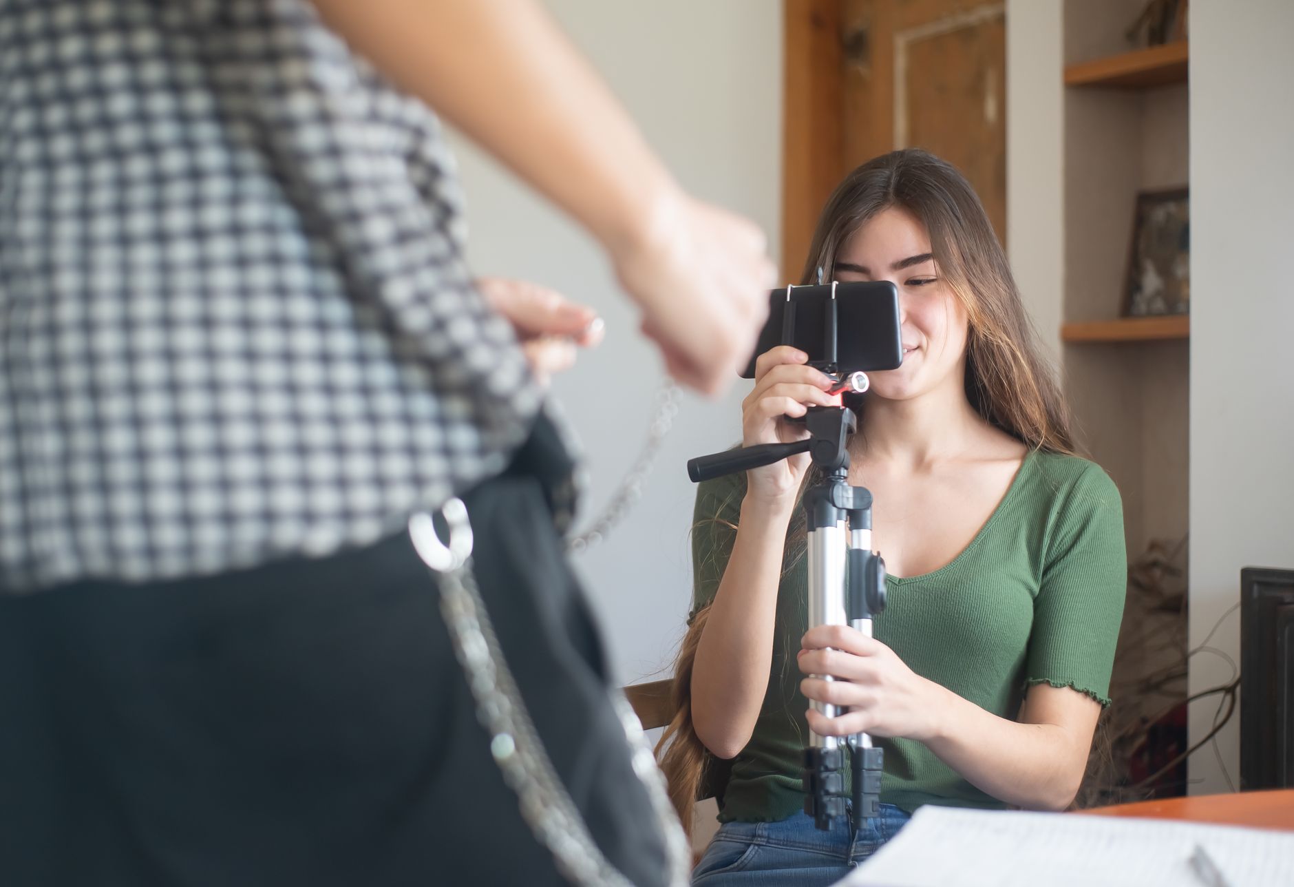A young woman films herself indoors, with a smartphone mounted on a small tripod for a video.