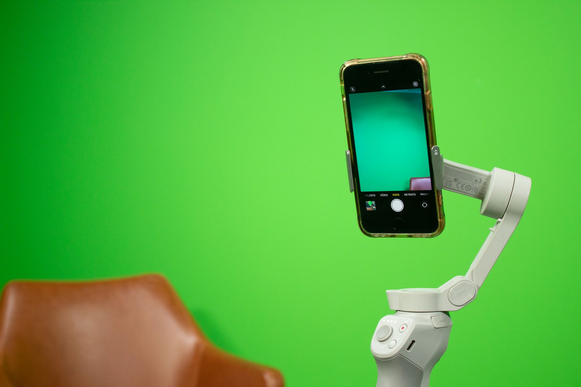A smartphone mounted on a small stabiliser gimbal in front of a green screen setup for video production.