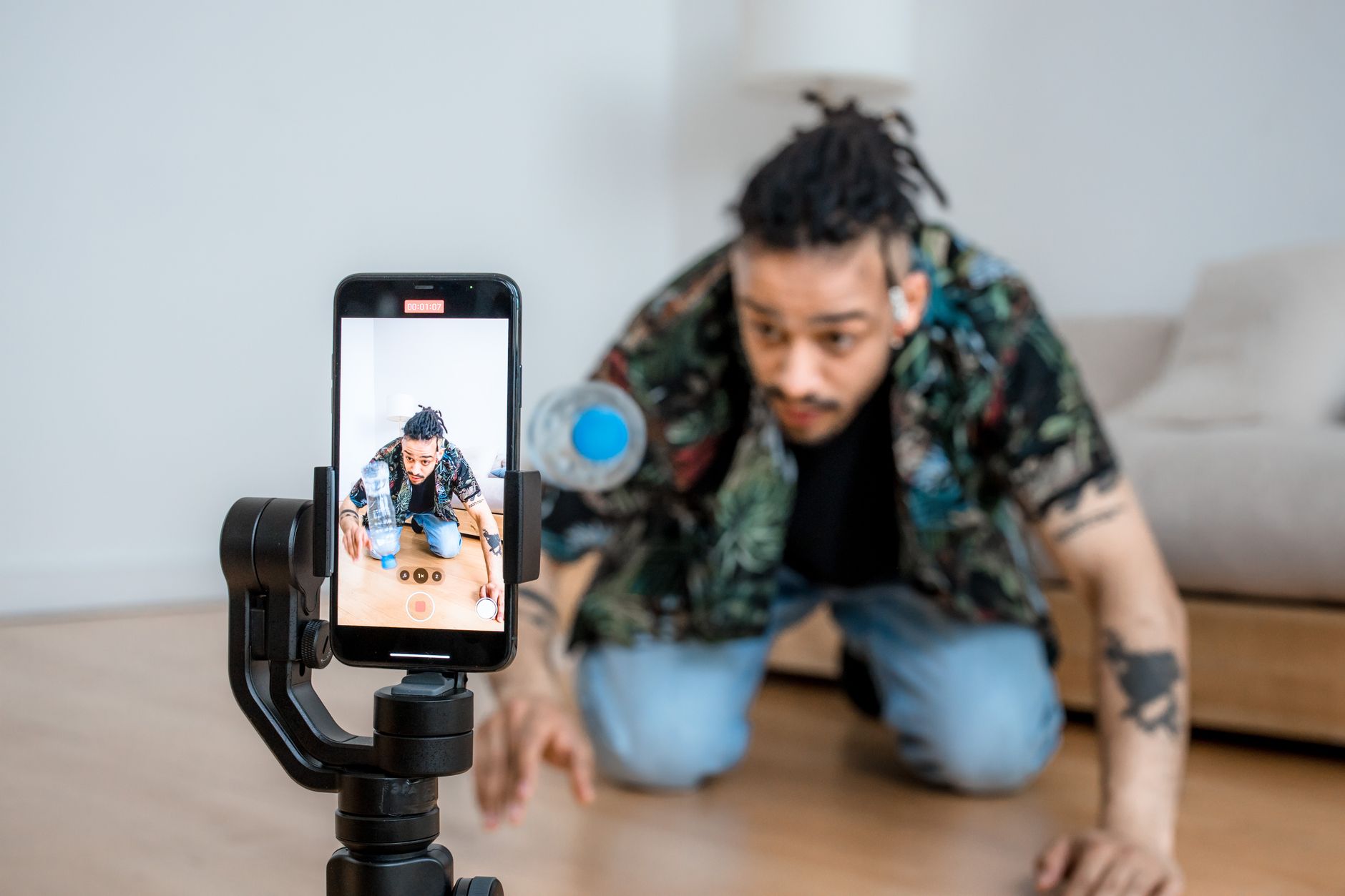A man films creative content with a smartphone mounted on a handheld gimbal indoors.