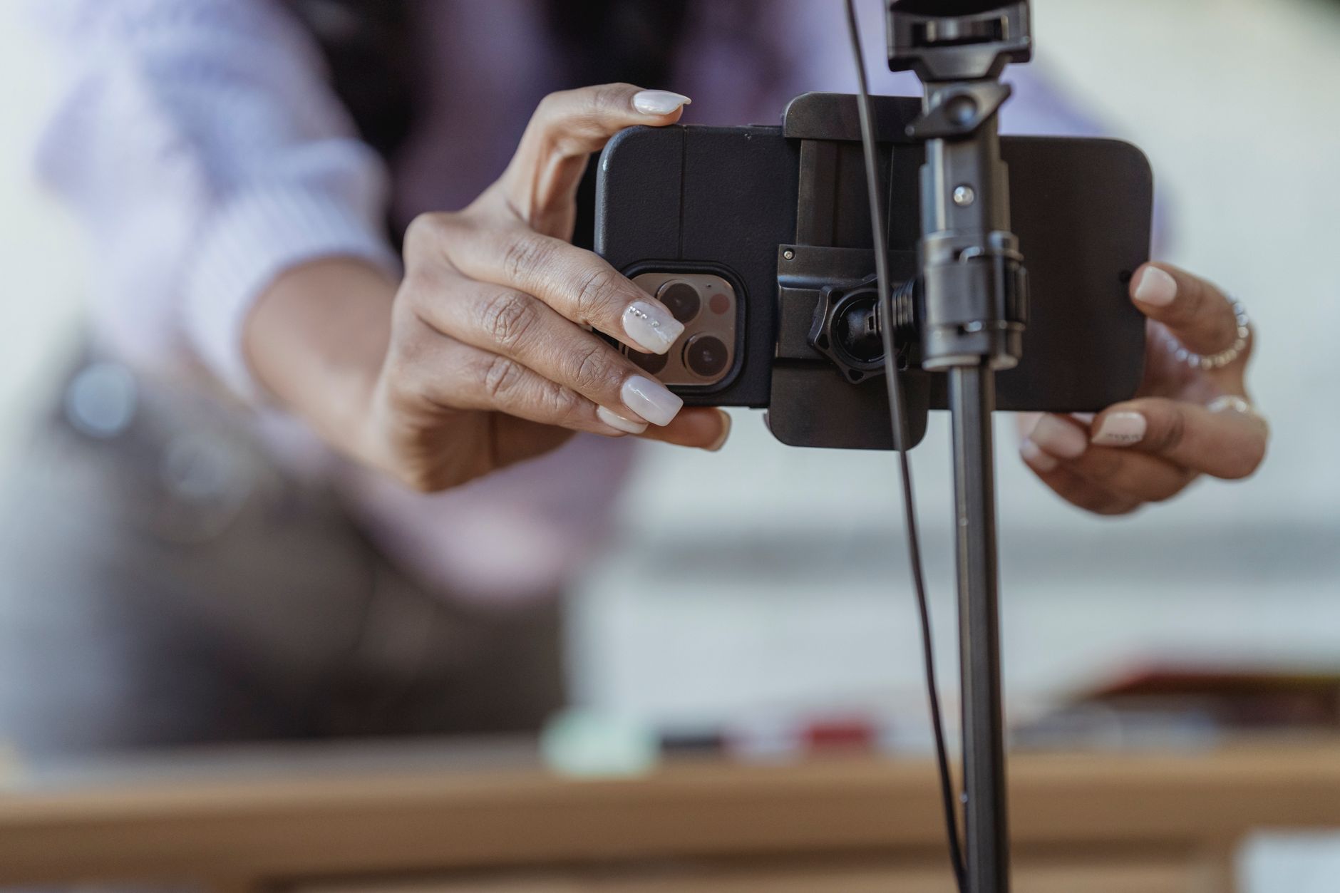 A close crop of a woman setting her mobile phone on a tripod while preparing to record a video, background blurred.